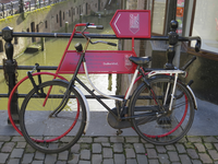 906788 Afbeelding van een fiets vastgezet tegen de reclamefiets 'Stadhuiskwartier' aan de reling van de Stadhuisbrug te ...
